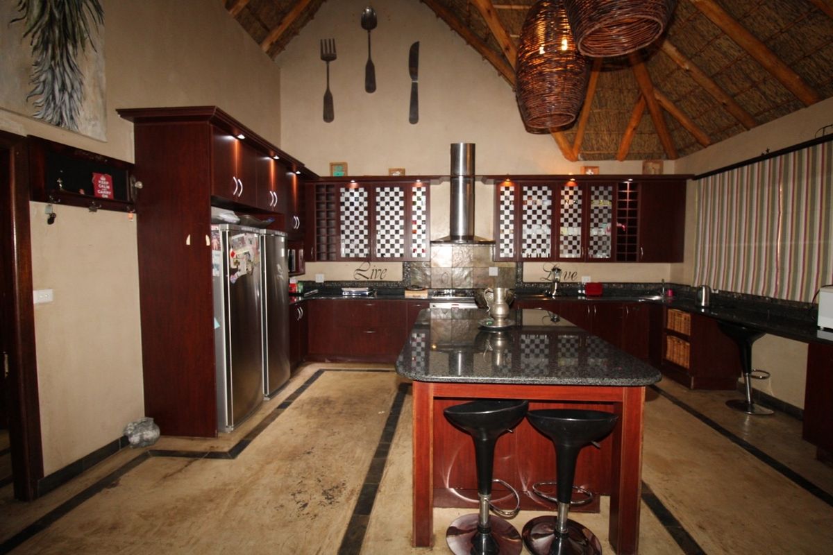 Spacious lodge-style kitchen featuring dark wood cabinetry, granite countertops, a central island, and a high vaulted ceiling with exposed thatch and timber rafters.