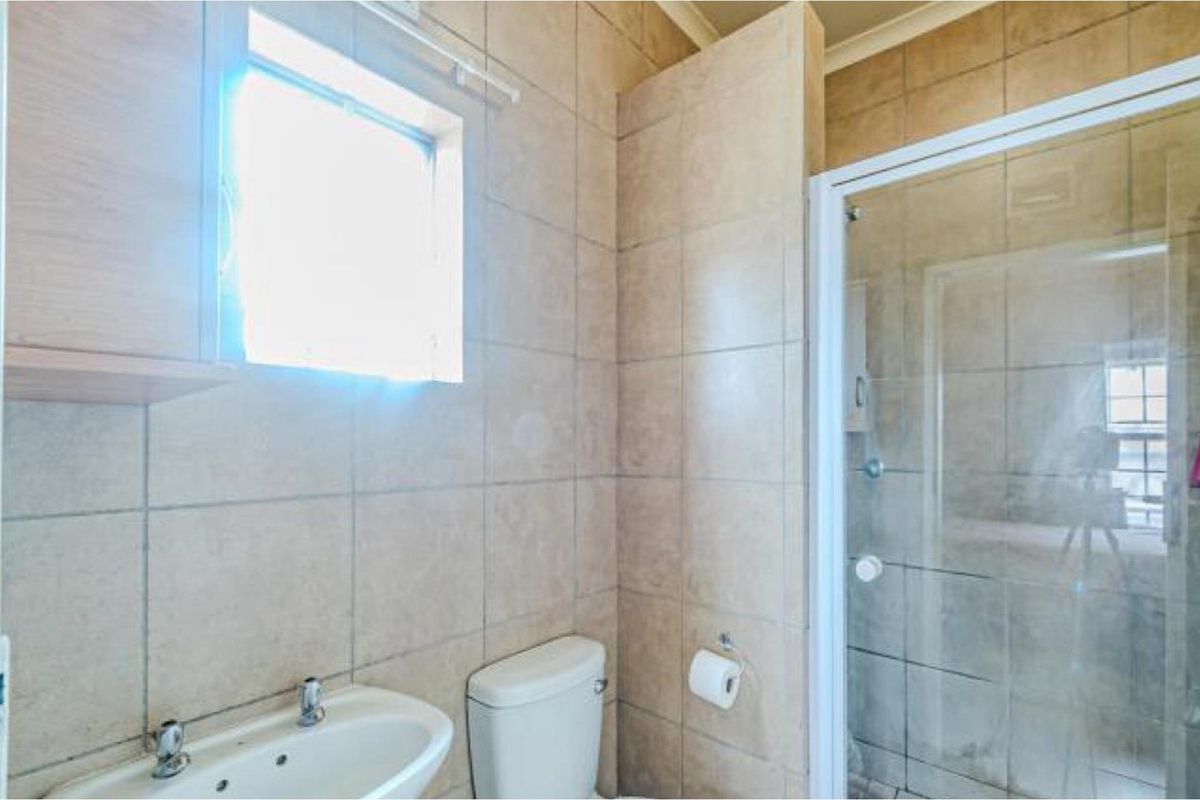 A functional bathroom featuring a glass-enclosed shower, wall-mounted basin, and toilet with neutral wall tiling.