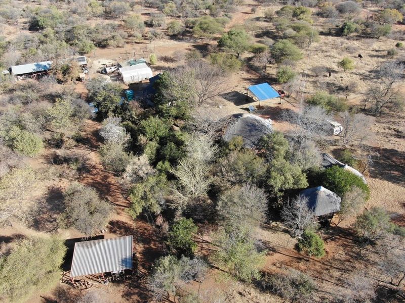 Aerial view of a rural farm property featuring multiple outbuildings, thatched roof structures, and extensive natural bushveld landscape.