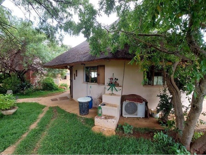 Exterior view of a thatched-roof farm building featuring a concrete pathway, integrated air conditioning unit, and surrounding garden area.