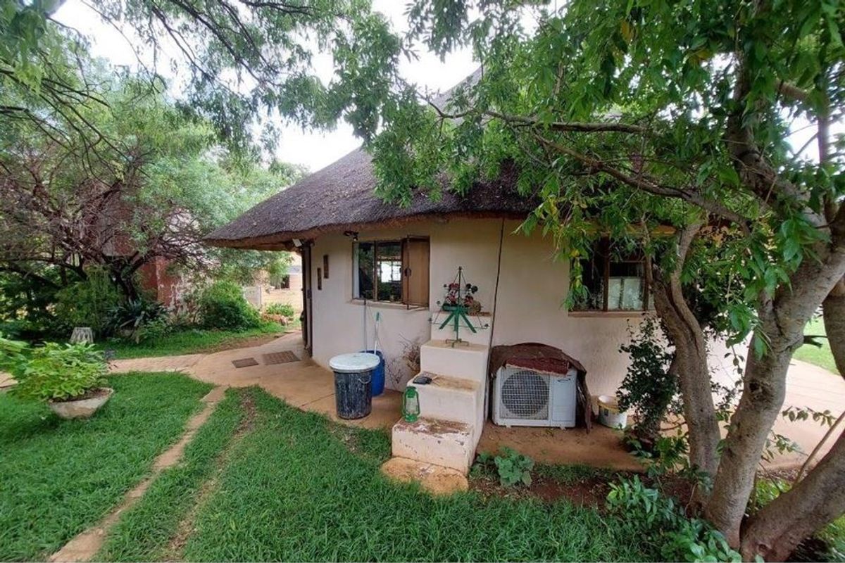 Exterior view of a thatched-roof farm building featuring a concrete pathway, integrated air conditioning unit, and surrounding garden area.