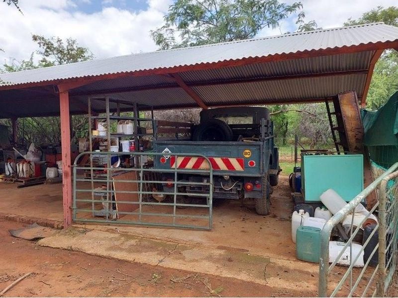 A functional open-sided farm utility shed with a corrugated metal roof, providing covered storage space for equipment and vehicles on the property.