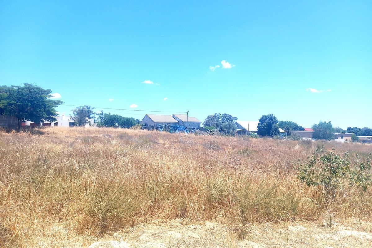 A view of a vacant residential plot featuring dry grass and surrounding neighborhood structures.
