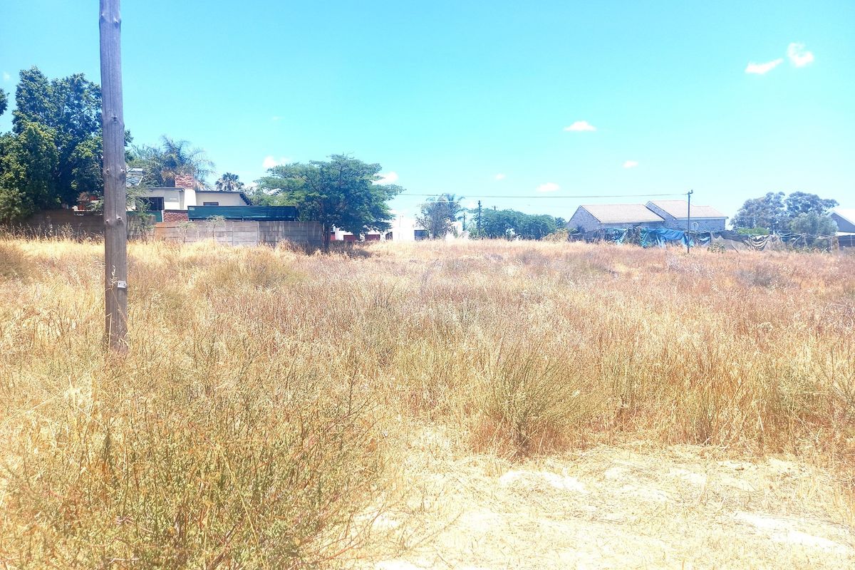 A vacant residential plot featuring dry grass and surrounding neighborhood views, offering a blank canvas for future development.