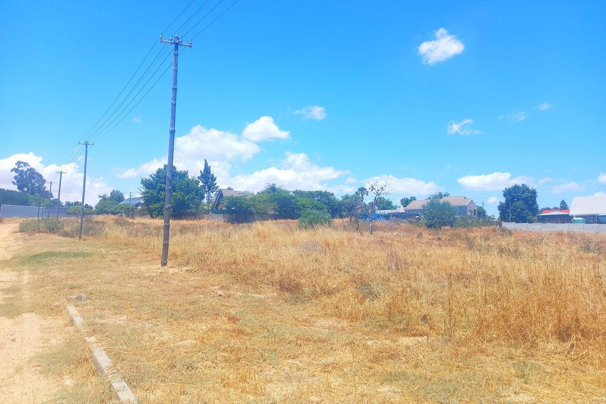 A view of a vacant residential plot featuring dry grass, utility poles, and surrounding neighborhood properties.