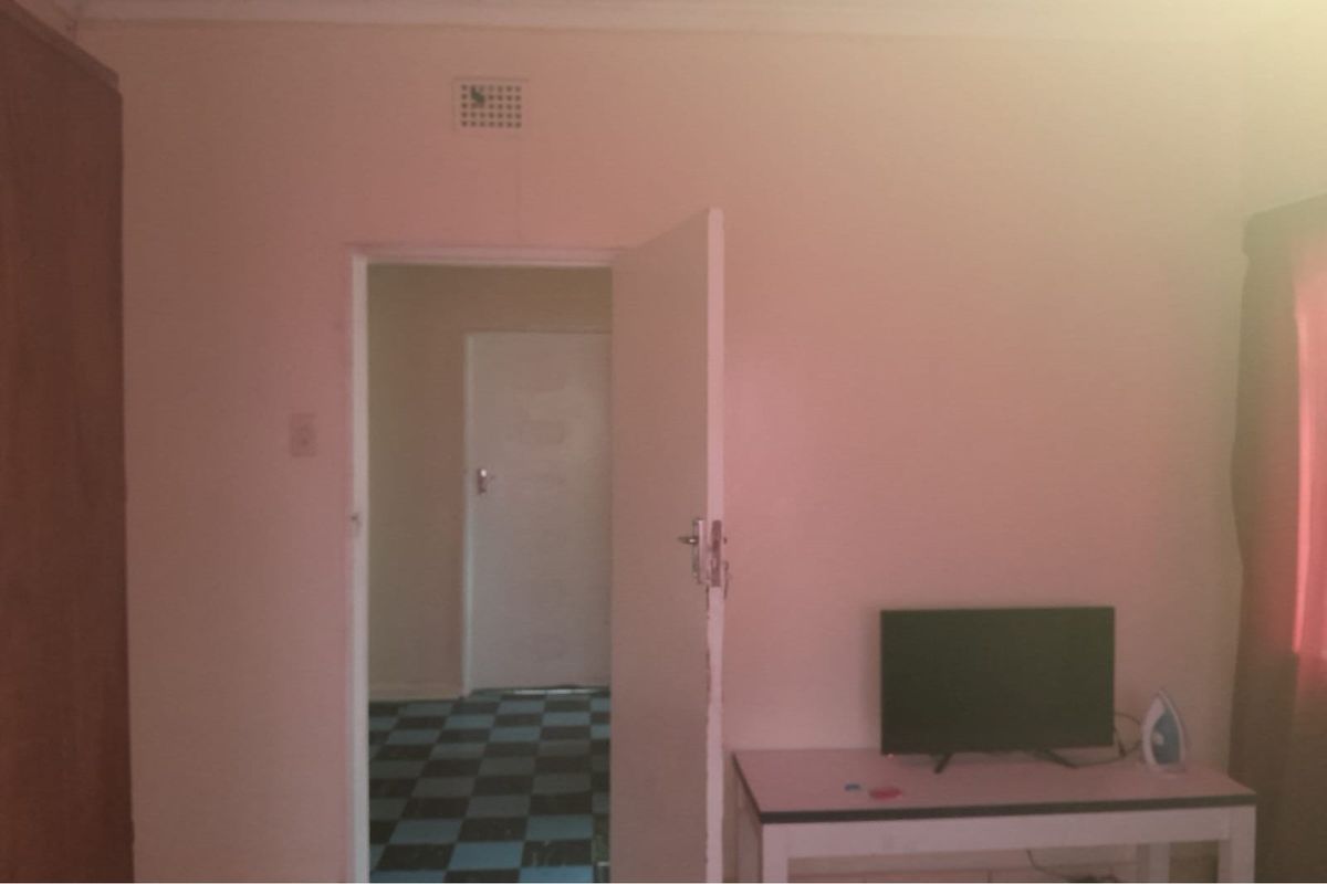 A bedroom interior featuring a built-in cupboard and a doorway leading to an adjacent room with checkered flooring.