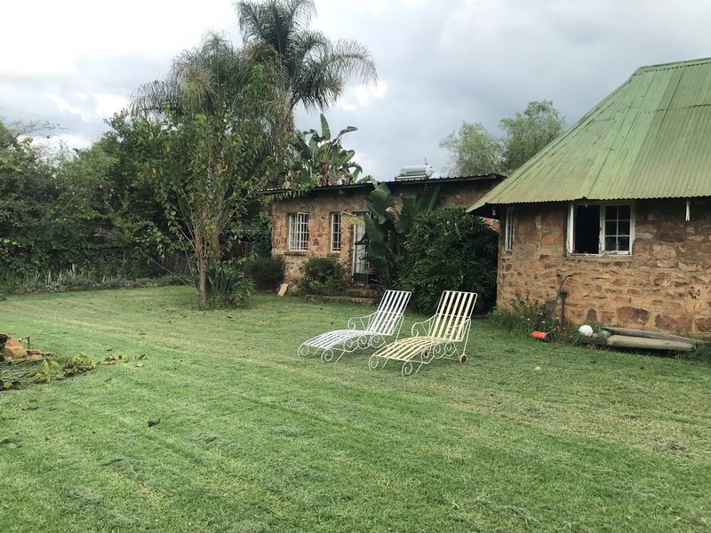 A rustic stone-walled cottage with a green corrugated metal roof, set within a spacious garden area on a small holding property.
