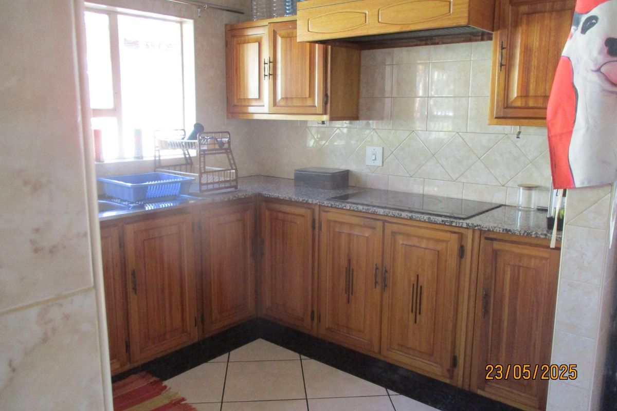 A functional kitchen featuring wooden cabinetry, granite countertops, a tiled backsplash, and a built-in hob with an extractor fan.