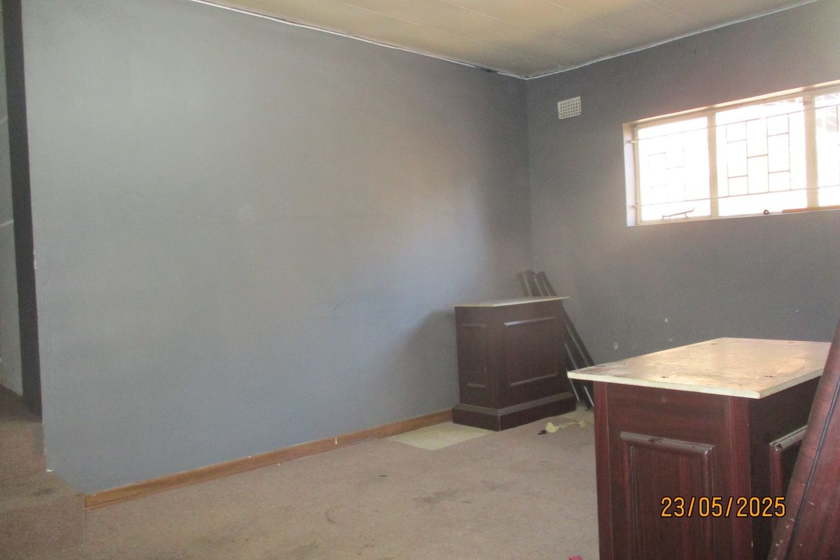 An empty living room featuring grey painted walls, carpeted flooring, and a window fitted with security bars.