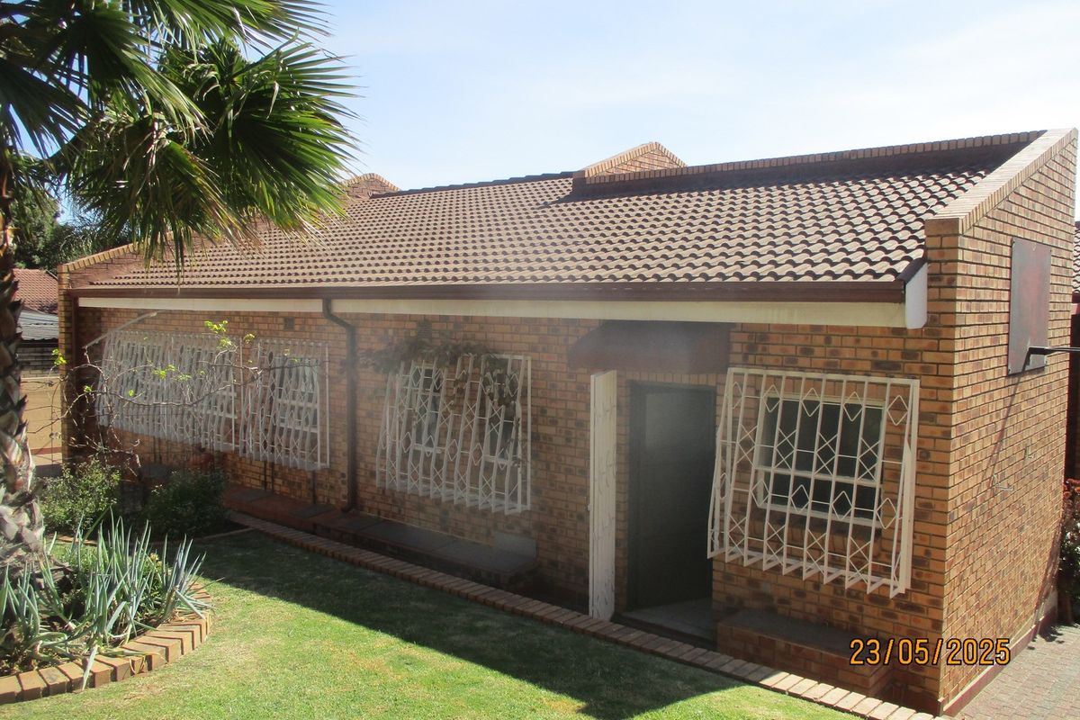 A rear view of a face brick house featuring a tiled roof and security bars on the windows, set against a small garden area.