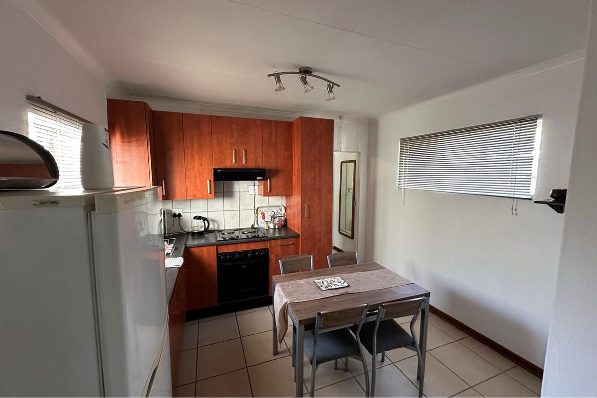 A functional kitchen featuring wood-finish cabinetry, a built-in oven and hob, extractor fan, and tiled flooring, with an adjacent dining area.