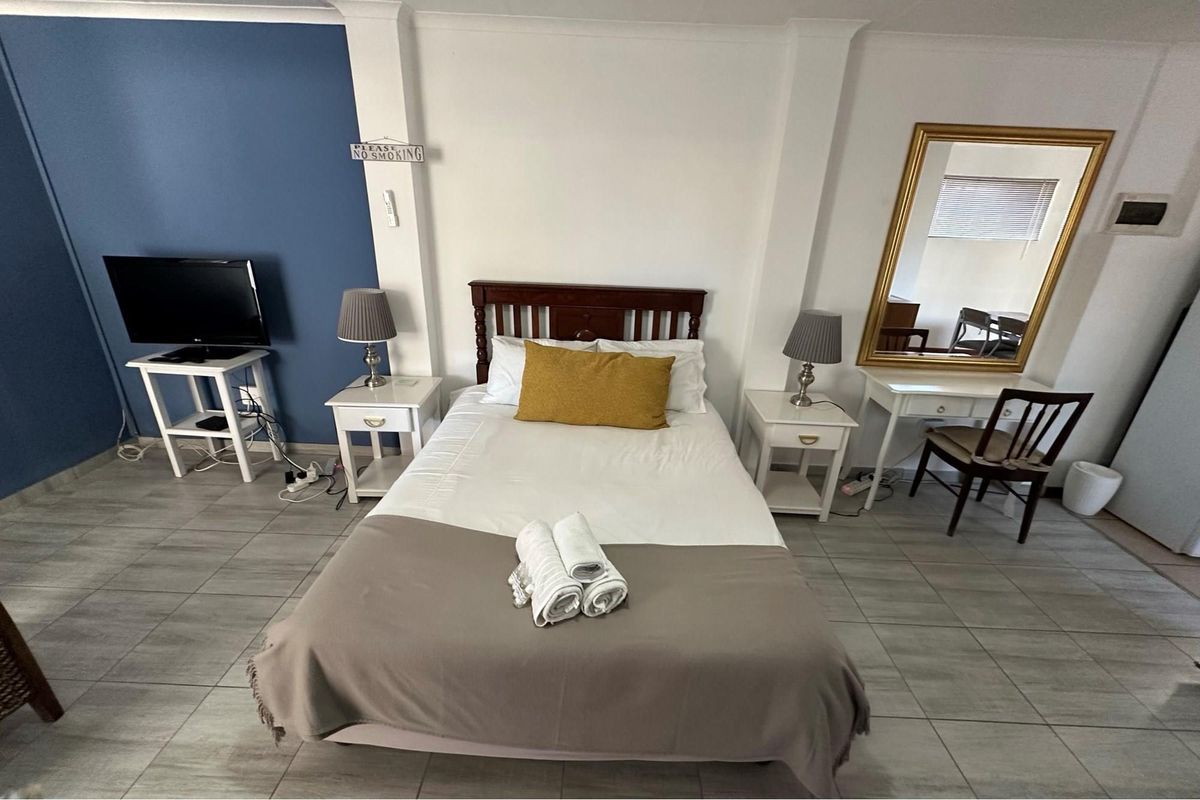 A bedroom featuring tiled flooring, a blue accent wall, and a built-in wall mirror.
