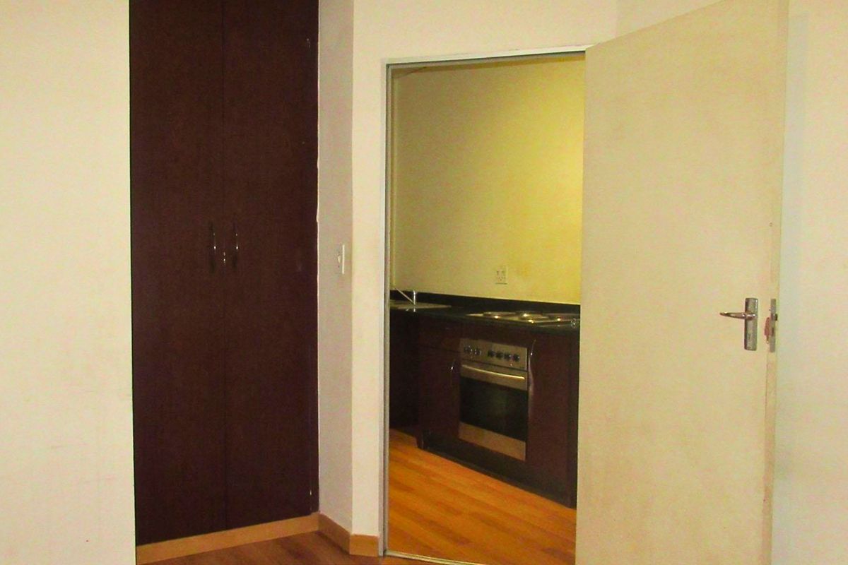 A bedroom featuring laminate flooring and a built-in cupboard, with a view through the doorway into an adjacent kitchen area.