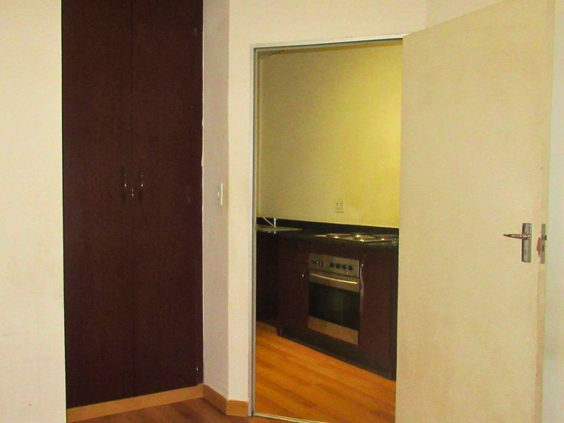 A bedroom featuring laminate flooring and a built-in cupboard, with a view through the doorway into an adjacent kitchen area.