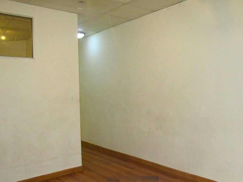 An empty hallway featuring laminate flooring and a small internal window, showing signs of wear on the wall surfaces.
