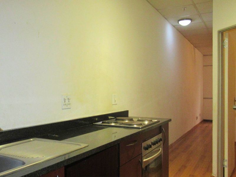 Compact kitchen area featuring a built-in oven, electric hob, stainless steel sink, and granite countertops, set within an open-plan layout.