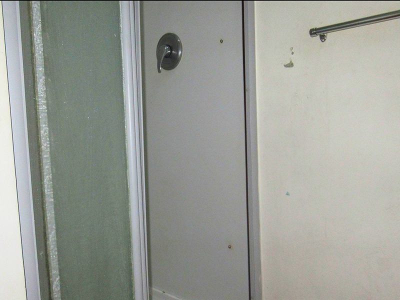 A compact bathroom featuring a shower enclosure and wall-mounted towel rail, currently showing signs of wear and requiring cosmetic attention.