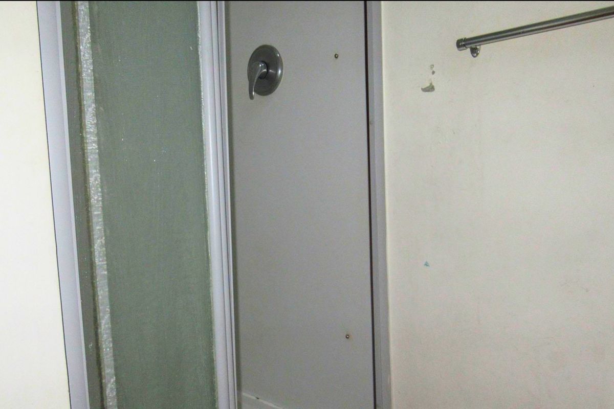 A compact bathroom featuring a shower enclosure and wall-mounted towel rail, currently showing signs of wear and requiring cosmetic attention.