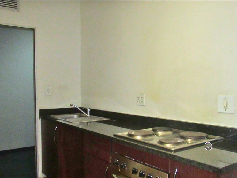 A compact kitchen featuring dark wood cabinetry, granite countertops, a built-in oven, and an electric hob.