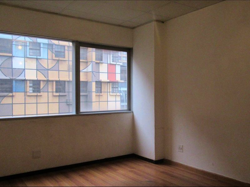 An empty bedroom featuring laminate flooring, a large window with urban views, and a drop ceiling, offering a blank canvas for renovation.