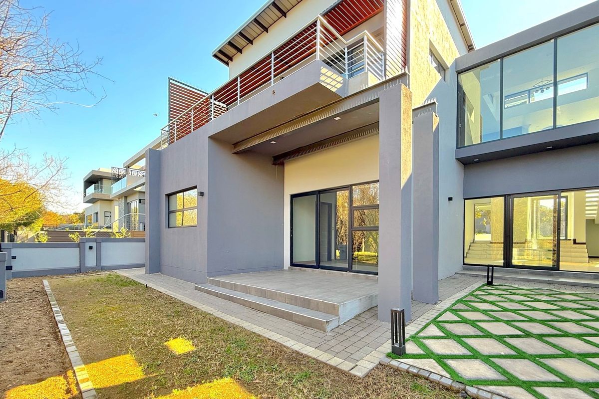 Modern rear exterior view featuring a covered patio, paved garden area, and a balcony with metal railings on the upper level.