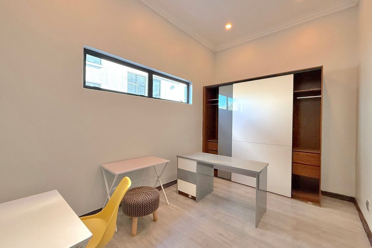 A bright bedroom featuring built-in sliding door wardrobes, modern laminate flooring, and a high-level horizontal window providing natural light.