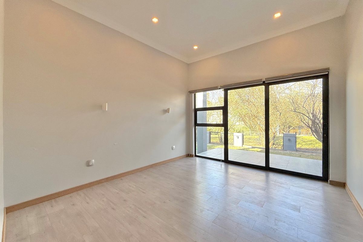 A bright, empty living room featuring light wood-look flooring, recessed ceiling lighting, and large sliding glass doors providing access to the outdoor patio area.