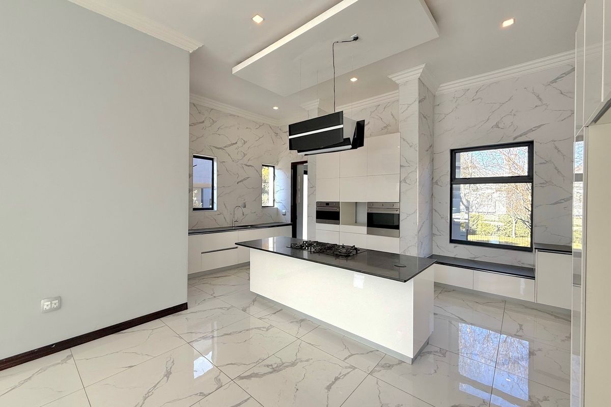 Modern kitchen featuring a central island with a gas hob, built-in ovens, marble-look tiled flooring, and sleek cabinetry with integrated lighting.