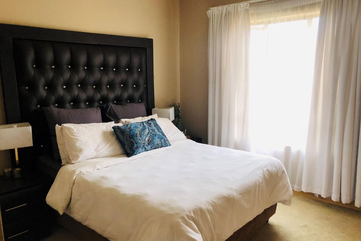 A comfortable bedroom featuring neutral wall tones, carpeted flooring, and a large window allowing for natural light.