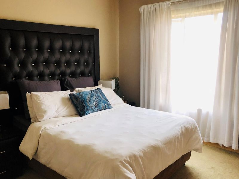 A comfortable bedroom featuring neutral wall tones, carpeted flooring, and a large window allowing for natural light.