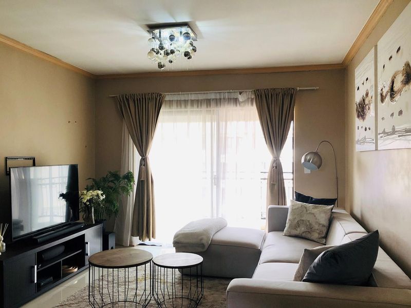 A cozy living room featuring tiled flooring, crown molding, and a sliding glass door that provides access to a balcony.