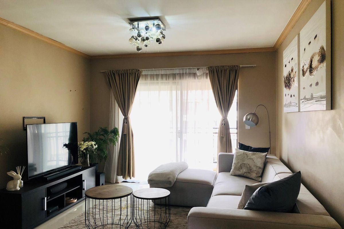 A cozy living room featuring tiled flooring, crown molding, and a sliding glass door that provides access to a balcony.