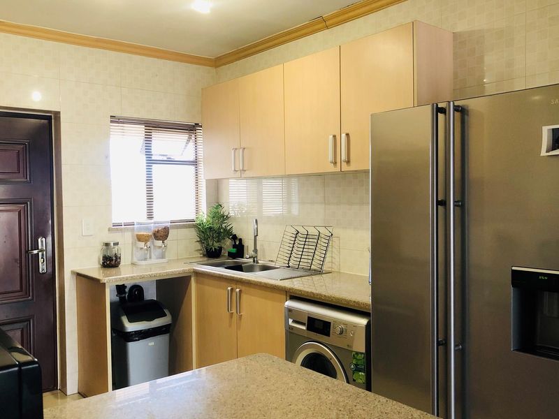 A functional kitchen featuring light wood cabinetry, granite countertops, tiled backsplash, and integrated space for a washing machine.