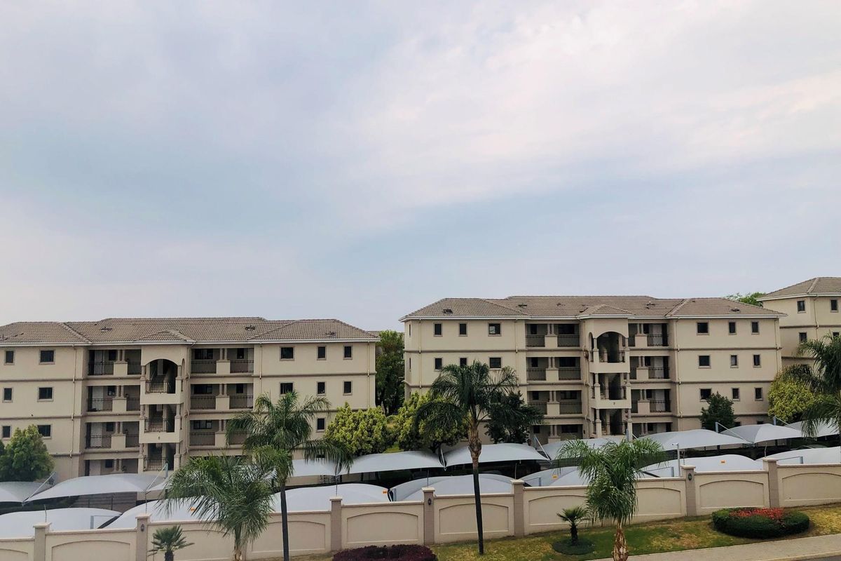 Exterior view of a multi-story apartment complex featuring tiled roofs, balconies, and covered parking bays within a landscaped residential estate.
