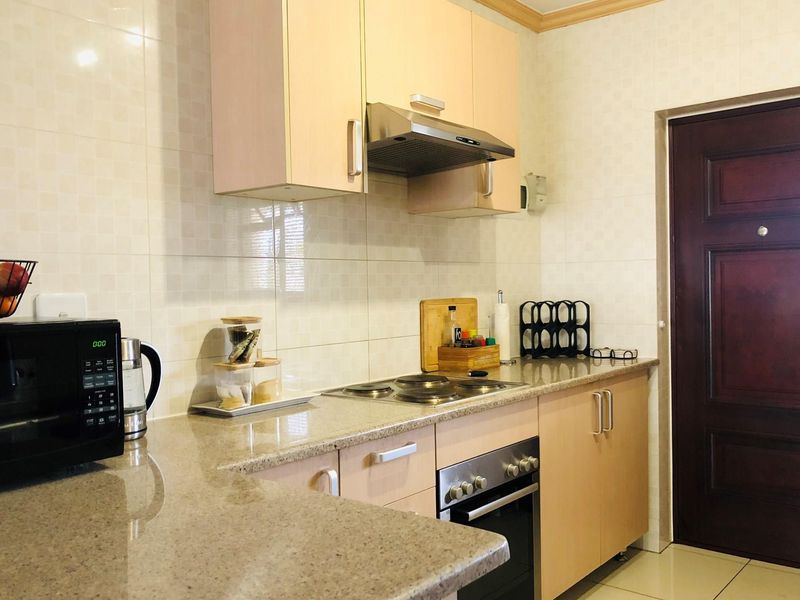 A functional kitchen featuring light wood cabinetry, granite countertops, a built-in oven, and an extractor fan, with tiled walls and flooring.