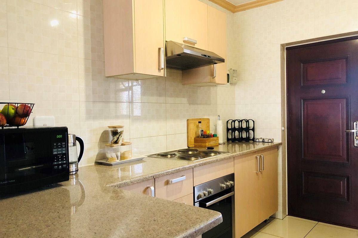 A functional kitchen featuring light wood cabinetry, granite countertops, a built-in oven, and an extractor fan, with tiled walls and flooring.