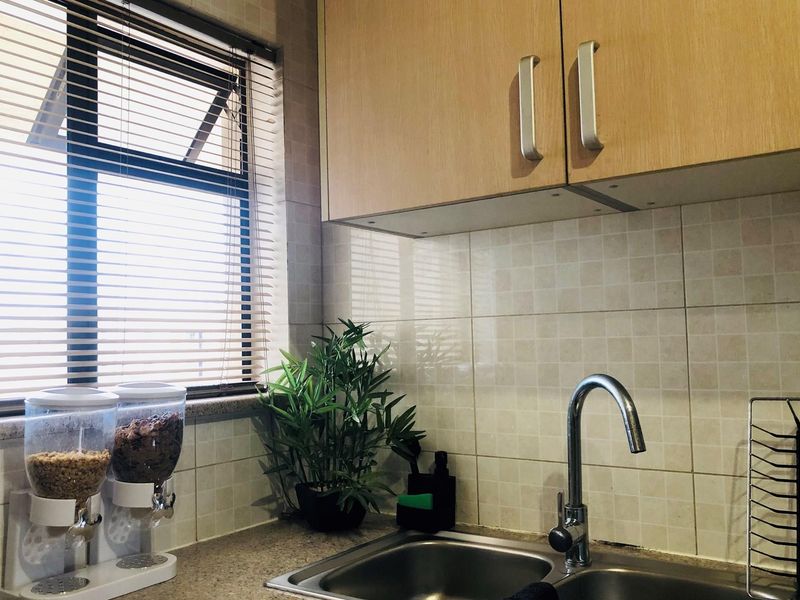 A functional kitchen area featuring light wood-finish cabinetry, tiled backsplash, a stainless steel double sink with a modern faucet, and a window with blinds.
