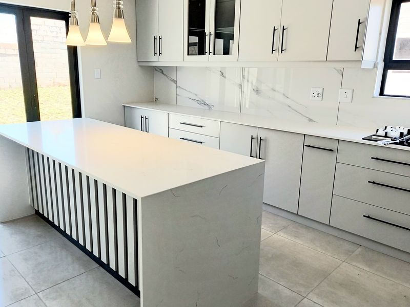 Modern kitchen featuring a central island with quartz countertops, marble-look splashback, sleek cabinetry, and integrated gas hob, offering a clean and contemporary aesthetic.