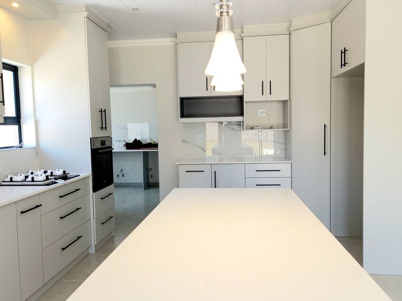 Modern, newly renovated kitchen featuring sleek cabinetry, stone countertops, a central island, and high-end built-in appliances with a clean, minimalist aesthetic.