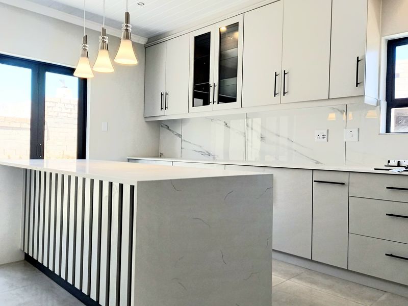 Modern kitchen featuring a large island with quartz countertops, marble-look splashback, sleek cabinetry, and contemporary pendant lighting, offering a clean and functional workspace.