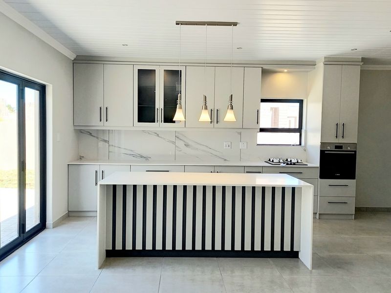 Modern kitchen featuring a central island, marble-look splashback, built-in oven, and sleek cabinetry, with direct access to the outdoors via bi-fold doors.