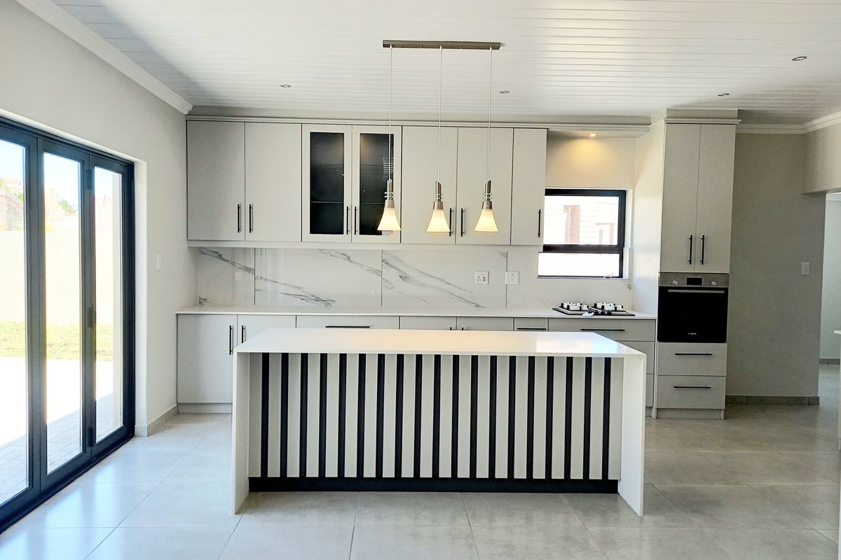 Modern kitchen featuring a central island, marble-look splashback, built-in oven, and sleek cabinetry, with direct access to the outdoors via bi-fold doors.