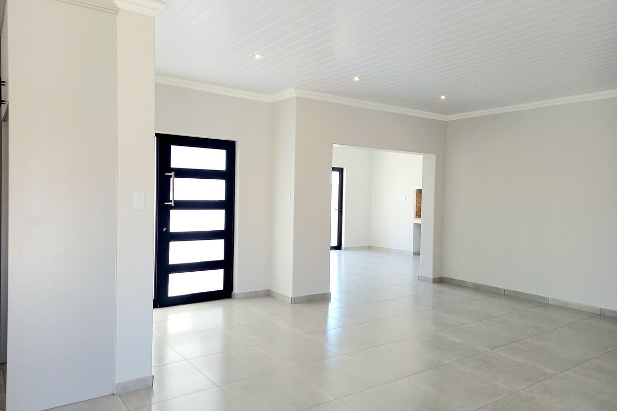 A bright, open-plan living area featuring neutral tiled flooring, a modern paneled front door, and a clean tongue and groove ceiling with recessed lighting.