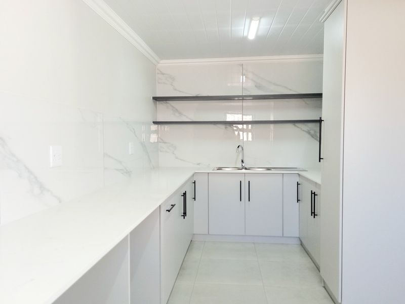 A modern, clean scullery featuring white cabinetry, marble-look splashbacks, open shelving, and a stainless steel sink, offering ample prep and storage space.