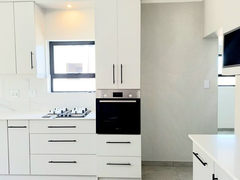 Modern kitchen featuring sleek white cabinetry, stone countertops, a built-in oven, and a gas hob with clean, contemporary finishes.