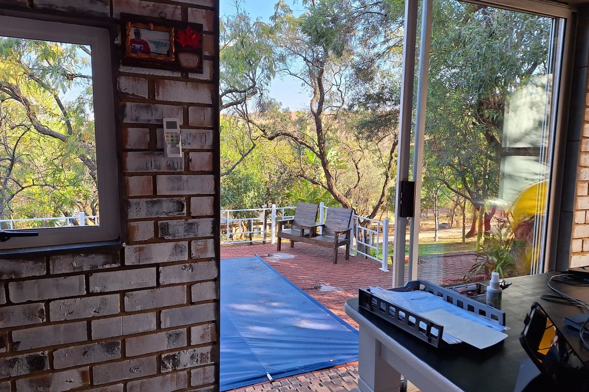 View from an interior space looking out onto a brick-paved patio area with a pool cover and surrounding garden trees.