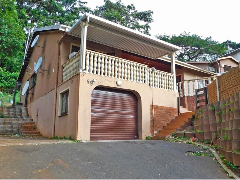 Front elevation of a multi-level house featuring a single garage, an elevated balcony with balustrades, and external concrete staircases.