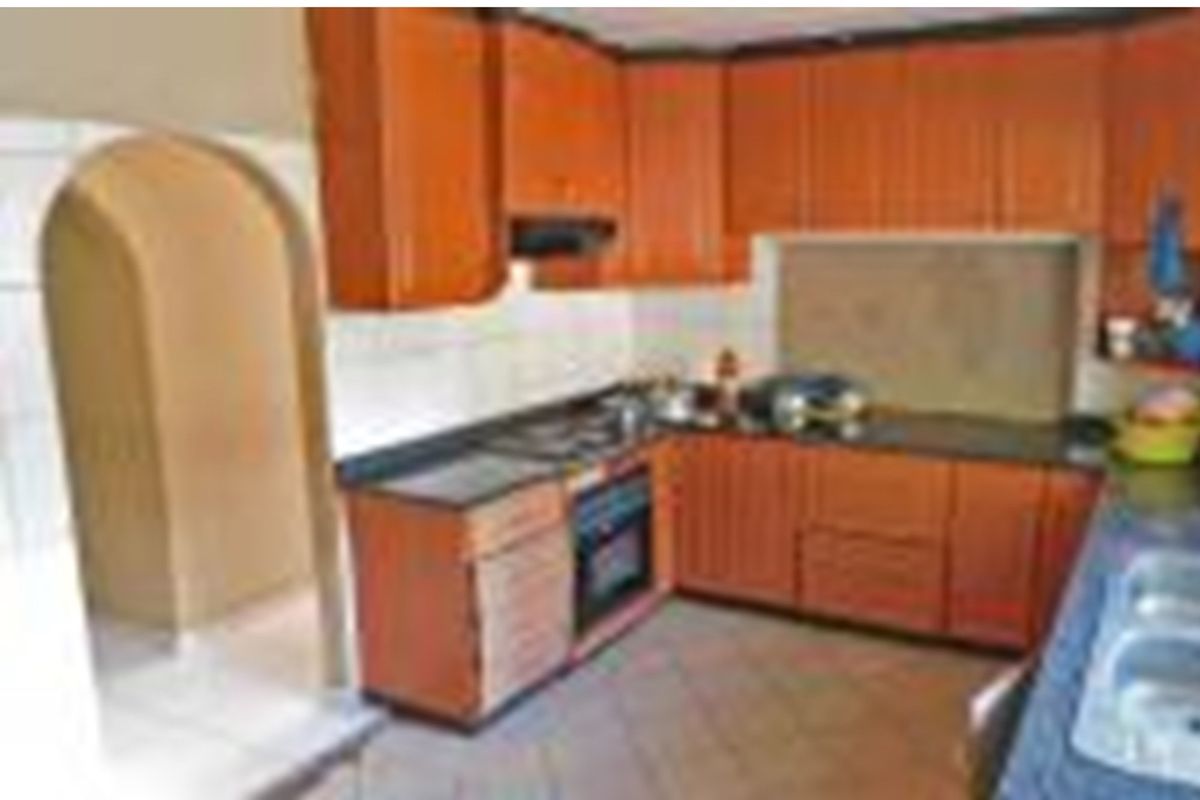 A functional kitchen featuring wood-tone cabinetry, built-in oven and hob, tiled backsplash, and an arched entryway leading to adjacent living spaces.