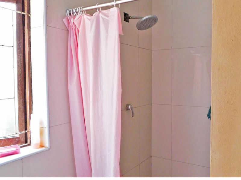 A functional bathroom shower area featuring tiled walls, a wall-mounted shower head, and a window for natural light.