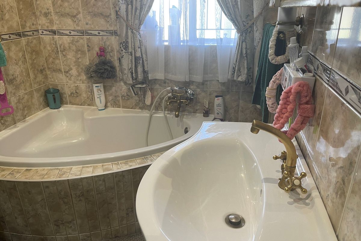 A compact bathroom featuring a corner bathtub, a pedestal basin with vintage-style brass taps, and full-height wall tiling.
